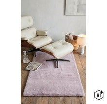 Un fotoliu confortabil cu taburet din piele și lemn așezat pe un covor pufos într-un living amenajat modern. (Image AI modified or generated)