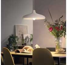 Lampă suspendată modernă deasupra unei mese de dining cu un buchet de flori și decorațiuni în fundal, într-o cameră luminoasă.