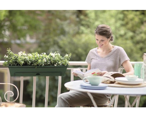 Femeie citind pe balcon cu jardinieră și masă aranjată