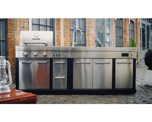 Bucătărie de exterior cu grătar, chiuvetă și dulapuri din oțel inoxidabil pe un fundal cu zid de cărămidă