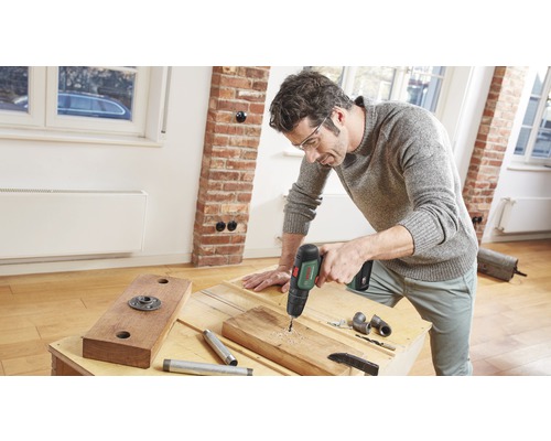 Un bărbat găurește o scândură de lemn cu o mașină de găurit.