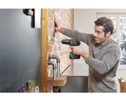 Bărbat găurind un zid de cărămidă cu o șurubelniță electrică