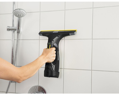 Mână care folosește aspiratorul de geamuri pe gresia de pe peretele băii