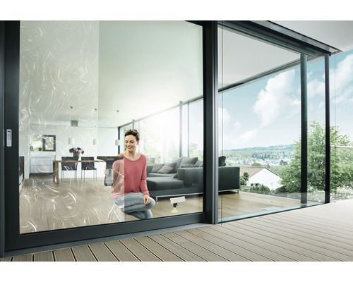 Femeie curăță ferestrele într-un living modern cu uși glisante din sticlă și terasă.