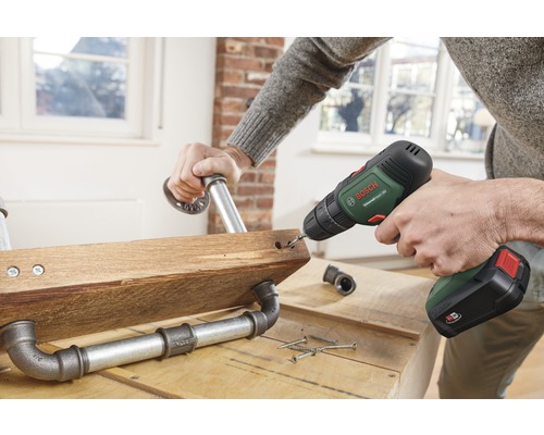 O persoană găurește o scândură de lemn cu fitinguri pentru țevi folosind o șurubelniță fără fir.