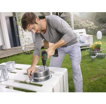 Bărbat găurind o găleată metalică în grădină cu o șurubelniță electrică.