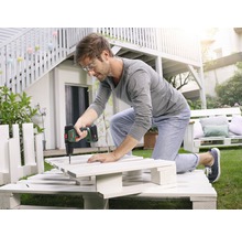 Un bărbat lucrează cu o șurubelniță cu acumulator la un proiect DIY din paleți în grădină.