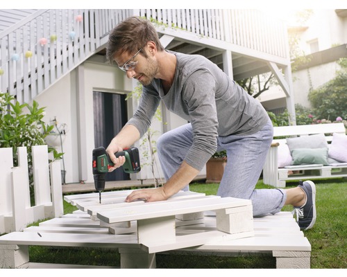 Un bărbat lucrează cu o șurubelniță cu acumulator la un proiect DIY din paleți în grădină.