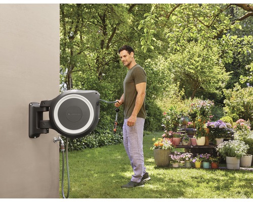 Un bărbat folosește un tambur pentru furtun Gardena montat pe perete în grădină