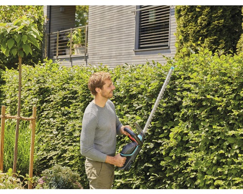 Un bărbat tunde un gard viu cu un tăietor de gard viu în grădină.