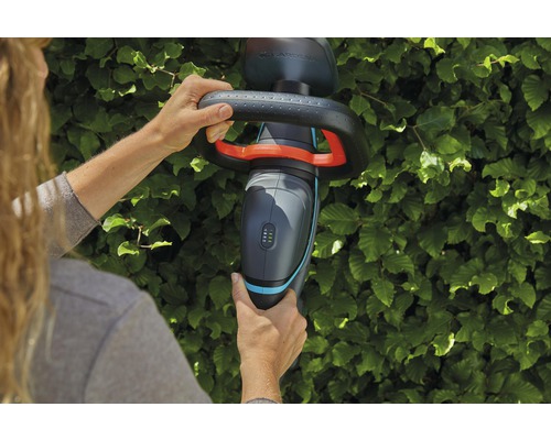 O persoană folosește un gard viu fără fir Gardena în fața unui gard viu.