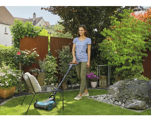 Femeie tunde gazonul cu o mașină de tuns iarba în grădină.