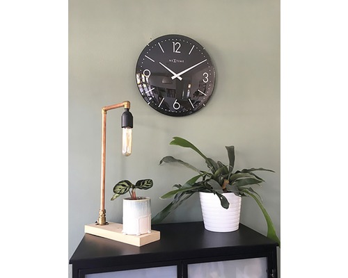 Ceas de perete negru lângă lampă de masă și plante de interior pe un dulap