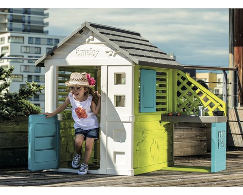 Copil se joacă într-o căsuță de joacă Smoby cu bucătărie și ușă