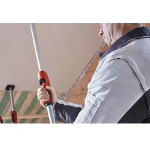 Un meșter folosește o tijă telescopică pentru a monta plăci de gips-carton pe un tavan.