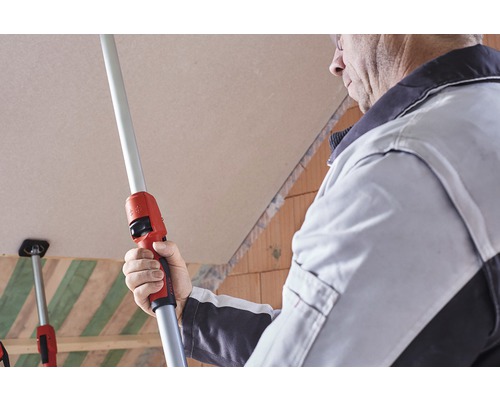 Un meșter folosește o tijă telescopică pentru a monta plăci de gips-carton pe un tavan.