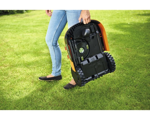 O persoană poartă un robot de tuns iarba peste un gazon.