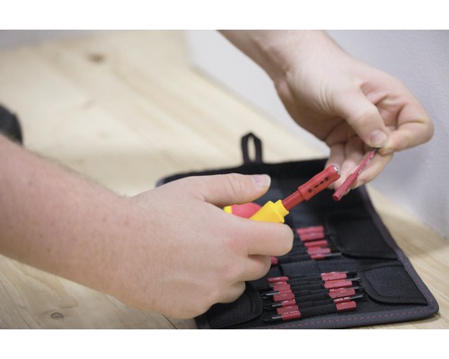 O persoană folosește un instrument de dezizolat pentru a dezizola un cablu în fața unei genți de scule