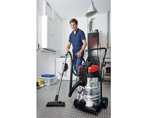 Un bărbat folosește un aspirator umed uscat într-o cameră cu mașină de spălat și uscător.