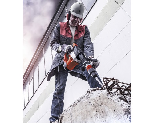 Un muncitor în construcții folosește un ciocan demolator pe beton, purtând echipament individual de protecție.