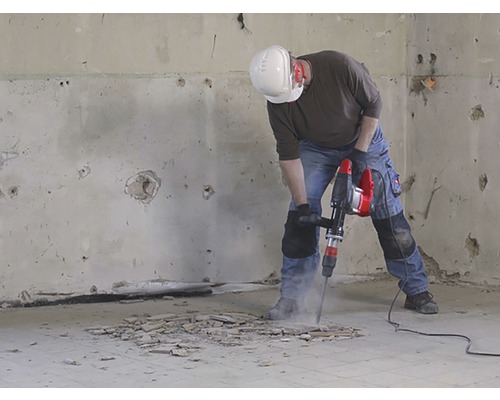 Un muncitor în construcții folosește un ciocan demolator pentru a lucra la podeaua dintr-o cameră.