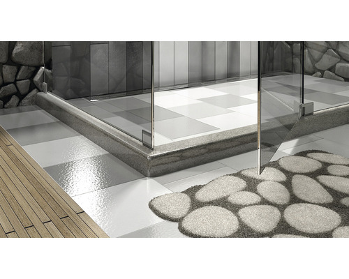 Prim-plan al unui duș cu ușă de sticlă, pereți decorați cu pietre și un covor de baie cu aspect de piatră