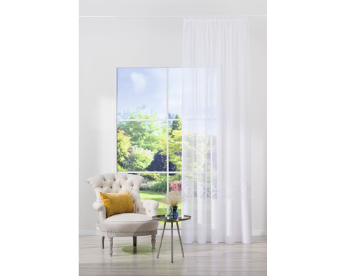 Cameră de zi luminoasă cu fotoliu, măsuță laterală și perdea în fața unei ferestre cu vedere spre grădină