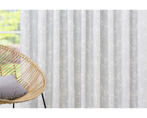 Șaluri decorative cu model floral în fața unei ferestre și a unui scaun de ratan.