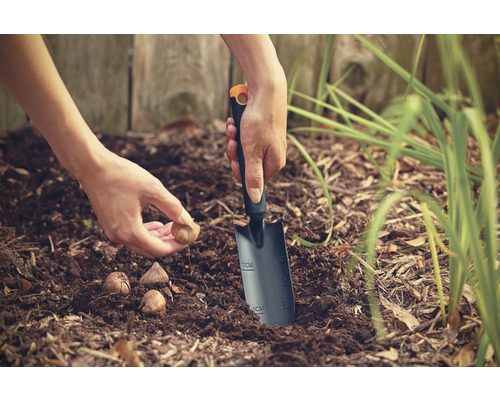 O persoană plantează bulbi de flori cu o lopată de plantat în grădină.