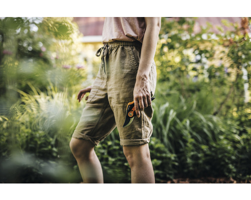 Femeie în grădină cu o foarfecă de grădinărit.