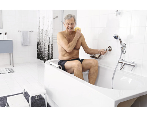 Un bărbat în vârstă folosește o cadă cu ajutor la intrare și bară de sprijin într-o baie luminoasă.