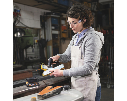 Femeie șlefuind o piesă metalică cu o unealtă de șlefuit într-un atelier