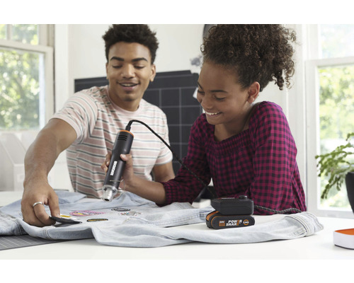 Două persoane atașează plasturi cu un pistol cu aer cald pe o țesătură de denim.