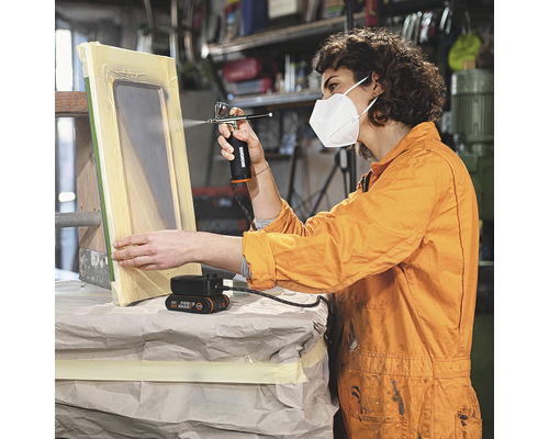 Femeie folosind un pistol de pulverizare a vopselei pentru a picta un cadru de fereastră