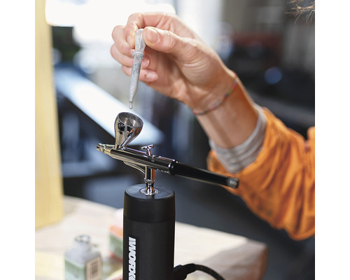 Persoană care umple un pistol airbrush cu o pipetă