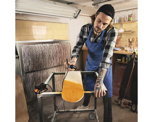 Un bărbat vopsește un skateboard cu un pistol de pulverizare a vopselei într-un atelier.