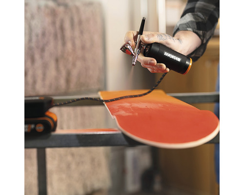 O persoană folosește un pistol de aerograf Worx pentru a picta o scândură de lemn.