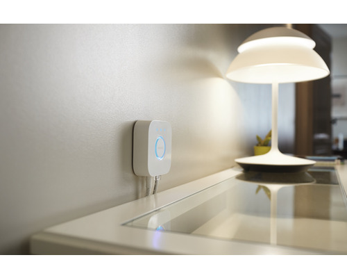Punte Philips Hue pentru controlul iluminatului inteligent pentru casă montată pe perete, lângă o lampă de masă.