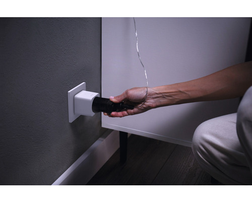 O persoană introduce o mufă neagră într-o priză albă în perete.