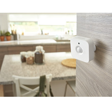 Senzor de mișcare Philips Hue alb montat pe o suprafață de lemn deschis într-o bucătărie luminoasă și organizată.