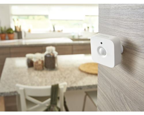 Senzor de mișcare Philips Hue alb montat pe o suprafață de lemn deschis într-o bucătărie luminoasă și organizată.