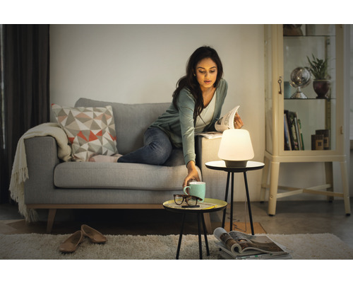 Femeie citind pe canapea lângă o lampă de masă și măsuțe laterale în camera de zi