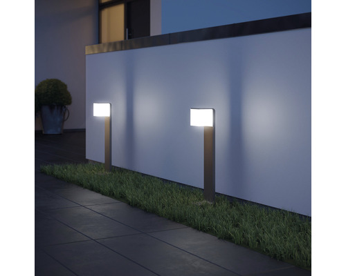 Două lămpi de grădină iluminează o potecă și un gazon în fața unui zid.