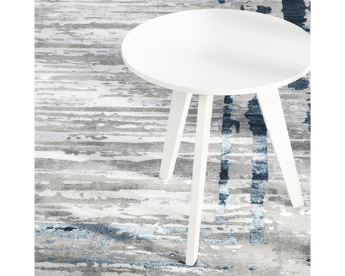 Măsuță laterală rotundă albă cu trei picioare pe un covor cu model