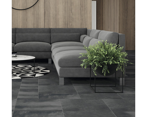 Living cu canapea de colț gri, plantă în ghiveci și covor geometric pe gresie închisă la culoare