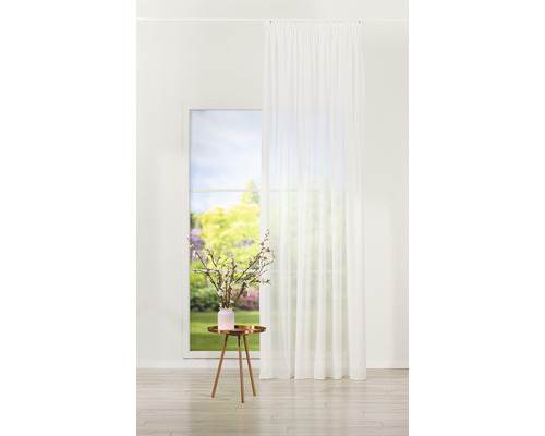 Perdea albă în fața unei ferestre cu vedere spre o grădină, lângă o masă cu o vază cu flori