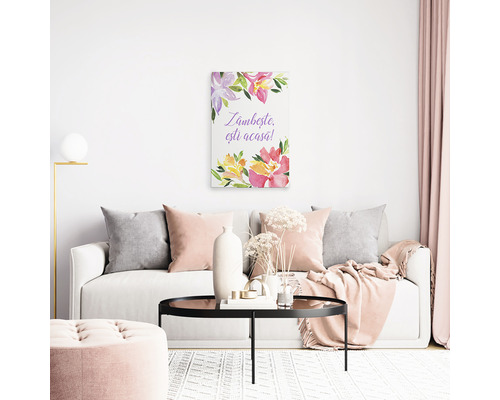 Pânză decorativă cu motiv floral și textul Zâmbește, ești acasă deasupra unei canapele