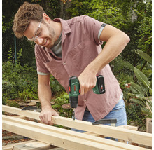 Un bărbat găurește o scândură de lemn cu o șurubelniță electrică fără fir