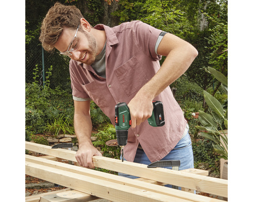 Un bărbat găurește o scândură de lemn cu o șurubelniță electrică fără fir