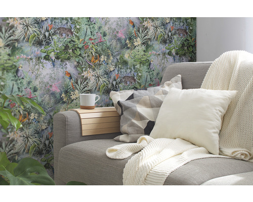 Cameră de zi cu canapea gri, perne și decorațiuni în fața unui tapet cu junglă